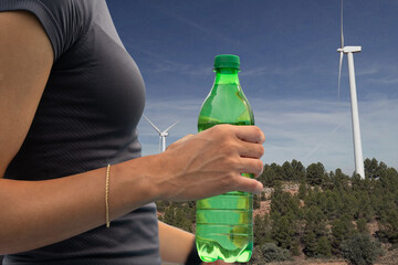 Woman holding a green bottle of water with wind turbines generating clean energy in the background