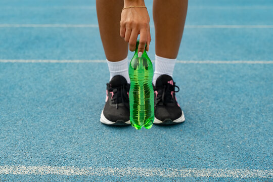 Athlete standing on a blue track, taking a hydration break from exercising