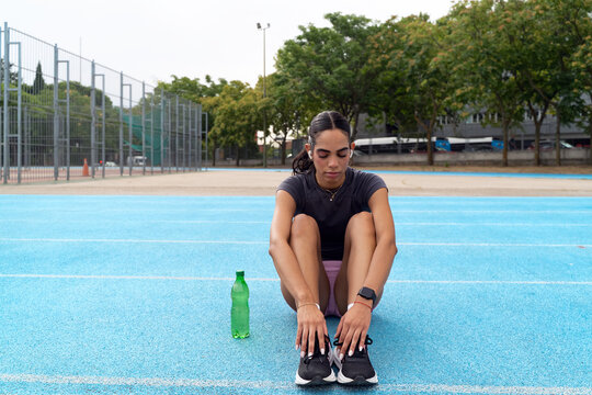 Young woman taking a break and hydrating on a blue athletic track