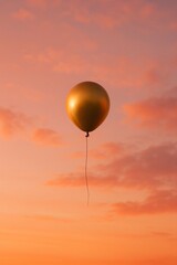 Fototapeta premium Gold balloon floating in pink and orange sunset sky
