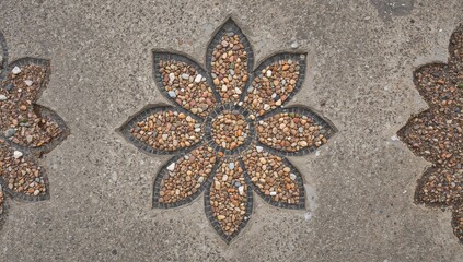 Close-up view of a flower-patterned mosaic crafted from colorful pebbles set into an aged concrete base, emphasizing artistic detail and rustic appeal