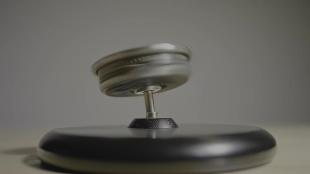 Motion-blurred metallic top spinning on a black base against a gray background