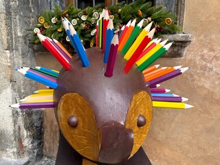 a colorful decorative sculpture resembling a hedgehog, with its spikes made from large, vibrant wooden pencils. The playful artwork has a brown body and a wooden face