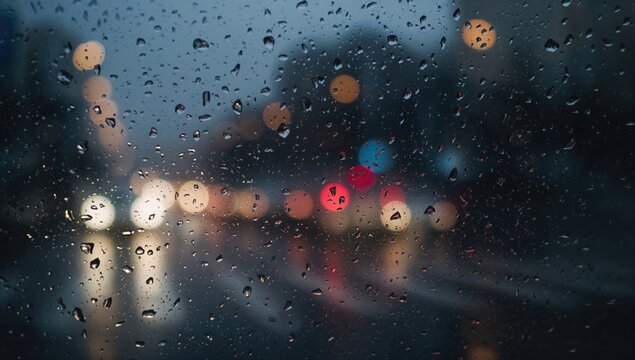 A blurred view of a rainy day with illuminated background lights, enhancing the feeling of movement and vibrancy