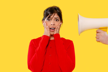 Woman in red sweater reacts to loud speaker on bright yellow background