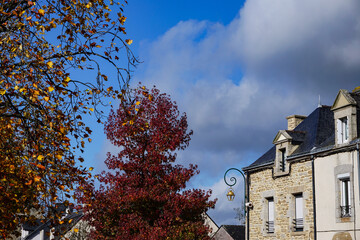 French village scene in autumn, with trees dressed in colorful leaves and old stone buildings against a bright blue sky, southern Brittany, France.