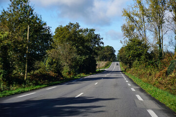 Scenic, tree-lined country road, Brittany, France, on a bright autumn day, offering travelers peace, seasonal beauty and leisurely touring, free from traffic and hurry.