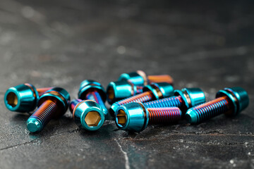 Blue titanium screws in a row with a hexagon head on a black textured background close-up