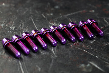 A series of titanium pink hexagon head screws on a black textured background close-up