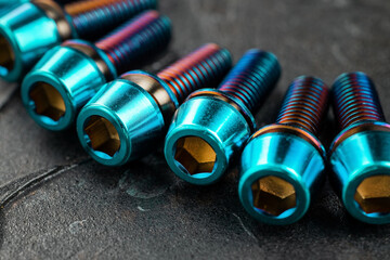 A series of titanium blue hexagon head screws on a black textured background close-up