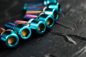 A series of titanium blue hexagon head screws on a black textured background close-up