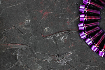 A series of titanium pink hexagon head screws on a black textured background close-up