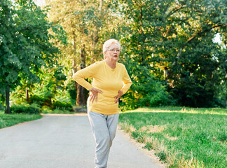 portrait of a senior woman exercising and running outdoors having chest or stomack or hip or back...