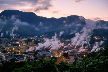 Beppu city in valley with smoke of hot spring bath houses at sunset, Oita
