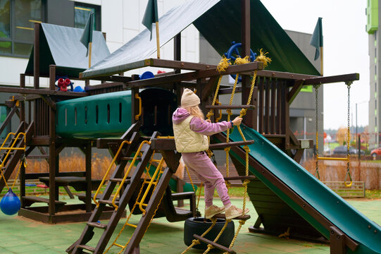child climbing outdoor playground structure in urban area. kid in warm outfit enjoying active play. modern residential neighborhood setting encourages physical activity and fun
