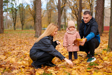 Fototapeta premium family enjoying autumn park together collecting leaves. woman, man, and child bonding in vibrant fall setting. cozy outdoor activity highlighting seasonal beauty and connection.