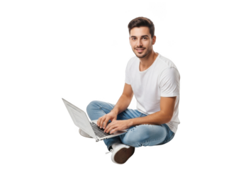 Smiling young man with beard wearing a white t shirt and blue jeans sitting cross legged typing on a laptop computer isolated on transparent background