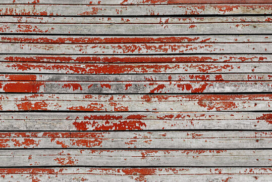Weathered wooden planks with peeling red paint, horizontal lines create rustic texture. Concept of vintage decay