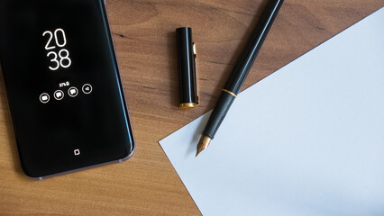 smartphone with ink pen and paper on the table.