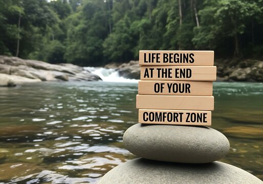 a serene river landscape provides a natural backdrop for stacked wooden blocks displaying an inspirational quote about leaving your comfort zone