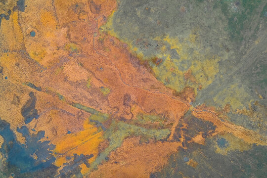Vibrant abstract aerial drone shot of a colorful swamp or mineral deposit. The rich orange, yellow, and green textures create a natural, painterly background for art, nature, or environmental concepts