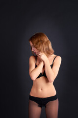 Fototapeta premium AIn the studio, against a black background, stands a beautiful and seductive girl in stockings and panties.