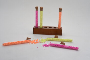 Yellow, pink and orange plastic granules in test tubes on a stand on white background