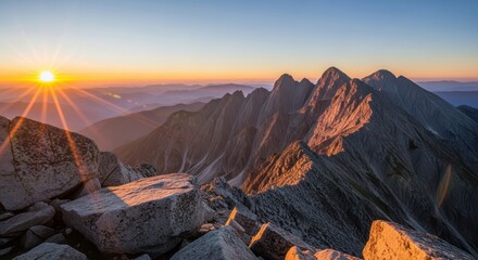 Fototapeta premium Sunrise over rugged mountain range with sharp peaks and rocky foreground, casting warm golden light and long shadows across the landscape at dawn
