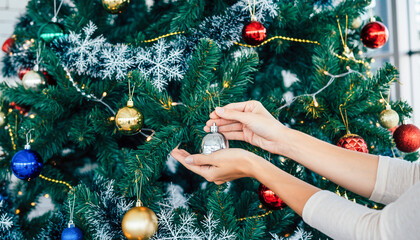 Female Hands Hanging Silver Ornament on Snowy Decorated Christmas Tree Branch