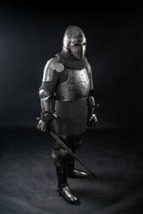 Portrait of a medieval knight in a closed helmet and a full set of armor with a sword in his hand isolated on a dark background