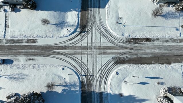 An aerial view of a snow-covered urban intersection in winter, showcasing a pristine white landscape with distinct vehicle tracks on the dark asphalt roads during a cold day
