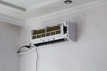 Wall-mounted air conditioner unit opened for repair and filter cleaning. Concept of home maintenance, energy efficiency, cooling system service, and air quality improvement.