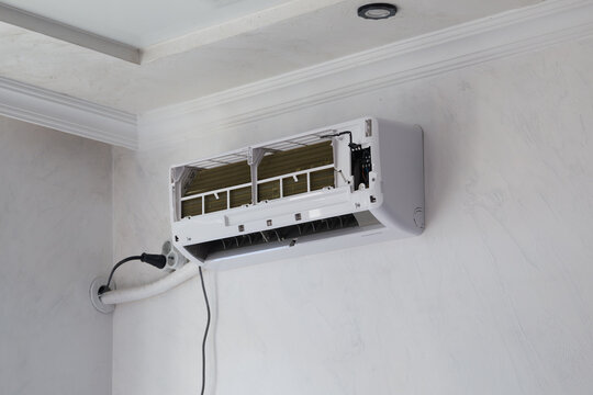 Wall-mounted air conditioner unit opened for repair and filter cleaning. Concept of home maintenance, energy efficiency, cooling system service, and air quality improvement.