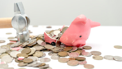 A broken piggy bank with coins and a hammer on the table