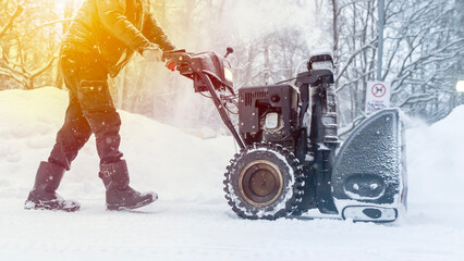 A man removes snow with a snow blower on the street