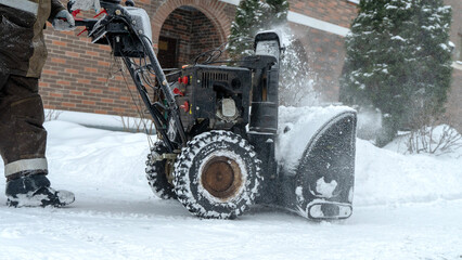 A man removes snow with a snow blower on the street