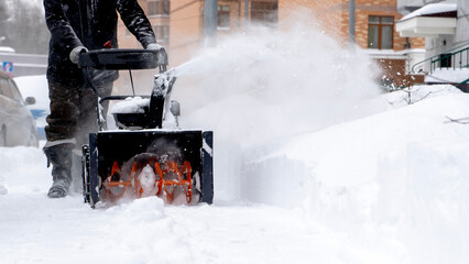 A man removes snow with a snow blower on the street