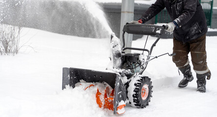 A man removes snow with a snow blower on the street