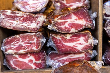 Vacuum-sealed cured meat pieces form layered stacks with rich marbling and deep color. market display shows texture, freshness and artisanal quality of traditional delicacy