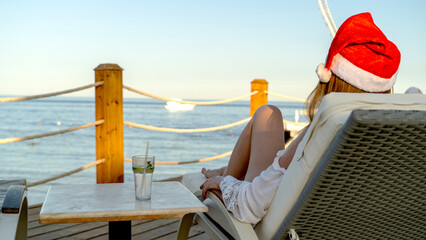 Woman in Santa's hat by the sea in a sun lounger