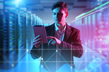 Data analyst monitors digital infrastructure using tablet in modern server room. Network management and cybersecurity operations in IT environment.