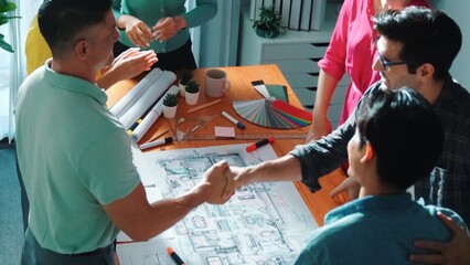 Top view of skilled business people shaking hands and making a contract. Aerial view of architect engineer working together and dealing plan or project at table with blueprint and notes. Symposium.
