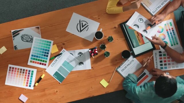 Top down aerial view of designer looking at tablet while project manager choosing color palettes. Top view of professional graphic designing and look at logo. Skilled team choosing graphic. Symposium.