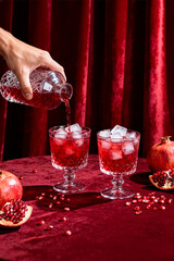Pouring vibrant pomegranate drinks into elegant glasses on a rich red table setting