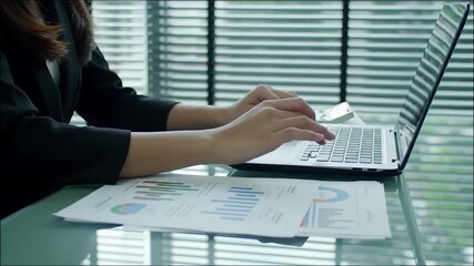 Close-up of hands typing on a laptop with financial charts and documents on a desk. Perfect for content about business, finance, remote work, productivity, and data analysis. - Powered by Adobe