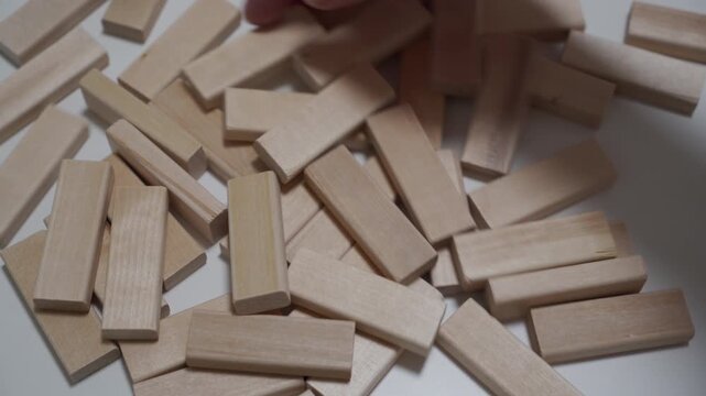 A pile of small, rectangular unfinished wooden blocks (like Jenga pieces) is quickly raked or mixed on a smooth white tabletop. The rapid movement generates a chaotic, loud clattering rattling sound