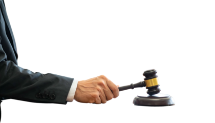 A person in a suit holds a wooden gavel. The background is black
