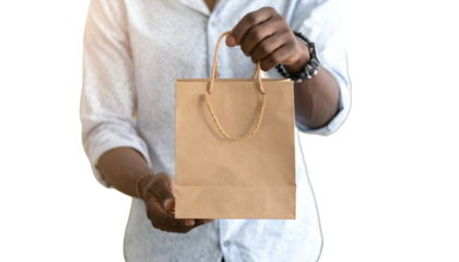 A person, likely a man, holds a small brown paper shopping bag, offering it to the viewer