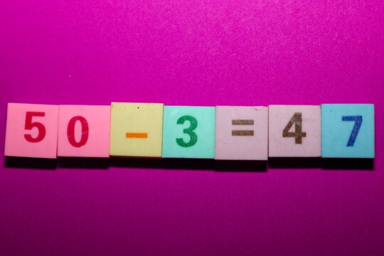 This close-up shot features the mathematical equation "50 - 3 = 47," spelled out using a row of multi-colored square tiles set against a vibrant magenta background.