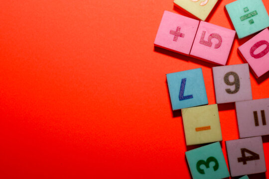 A vibrant orange background provides a strong contrast for a cluster of colorful square tiles arranged in the bottom-right corner of the frame. The tiles feature embossed numbers, letters, and mathema